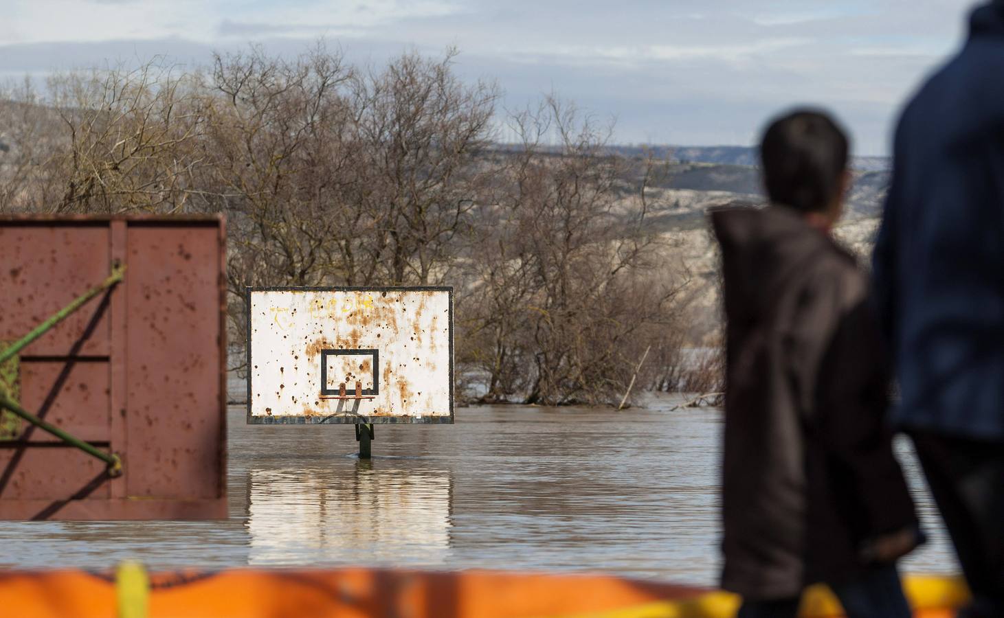 Varias personas observan un campo de baloncesto anegado por la crecida del río Ebro, hoy en la localidad de Cabañas de Ebro.