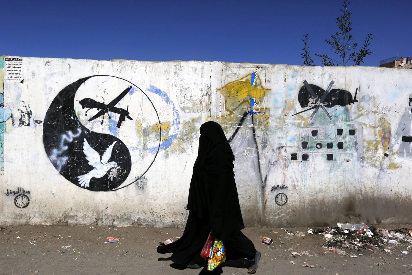 Pintada contra el uso de drones en Yemen. Una mujer yemení pasa junto a un grafiti de protesta contra los drones estadounidenses que intervienen en la guerra contra Al Qaeda en la Península Arábiga (AQPA), la filial de Al Qaeda en Yemen. Estados Unidos realiza desde hace años operaciones con drones en Yemen contra Al Qaeda, una estrategia a la que se sumó a principios de 2016 Arabia Saudí, también con aviones no tripulados. EFE/YAHYA ARHAB