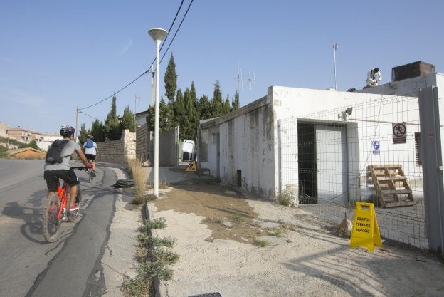 Unos ciclistas pasan junto al pozo que abastece la urbanización de Calicanto. 