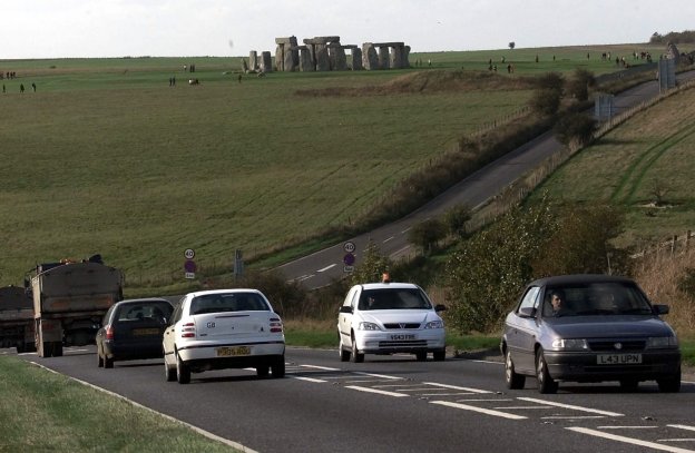 Los vehículos circulan por la carretera próxima a Stonehenge, que se recorta contra el horizonte. 