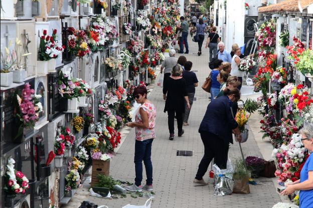 Diversas personas pasan por una de las calles del cementerio de Dénia mientras otras preparan las flores. 