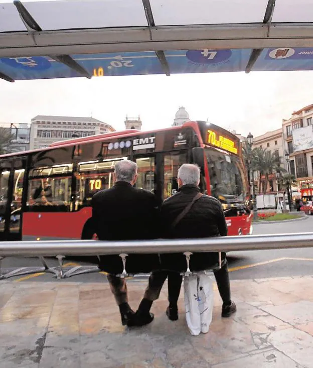 Vecinos esperan un autobús en una parada de la plaza de la Reina. 