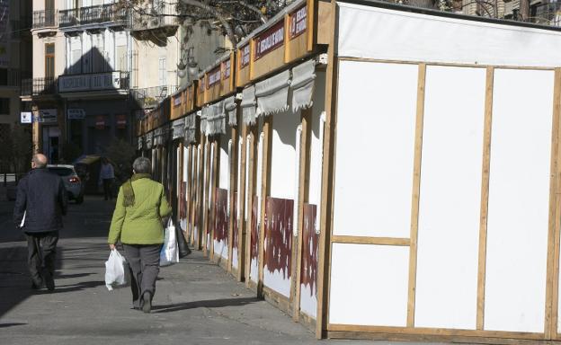 Viandantes pasean por la calzada entre las casetas vacías. 