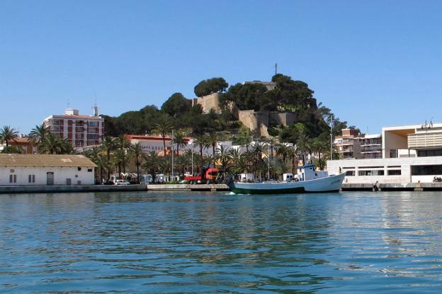 El castillo de Dénia, cubierto en gran parte de árboles, visto desde la zona portuaria de la ciudad. 