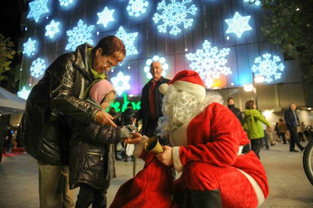 Un Papá Noel entrega un regalo a una niña a las puertas de unos grandes almacenes. 