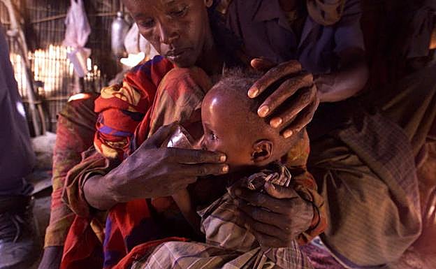 Un niño etíope bebe agua en brazos de su madre.