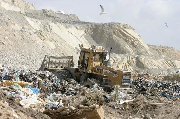 Una máquina excavadora trabaja en un vertedero. 