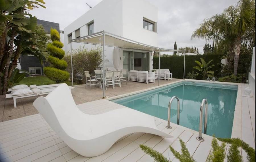 En la zona exterior, la terraza está a ras de vivienda y se presenta como una continuidad visual del interior. Allí, en la zona de comedor y descanso, el suelo está cubierto de baldosas y junto a la piscina de un porcelánico blanco emula la tarima de madera.