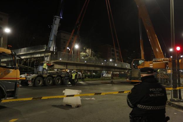 Un policía observa como los operarios cargan, anoche, una de las pasarelas con la ayuda de una enorme grúa. 