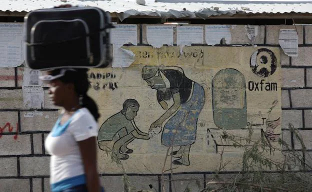Una mujer camina junto a un mural de Oxfam. 
