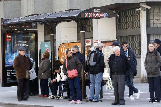 Más de una decena de personas esperan en una parada del autobús. 