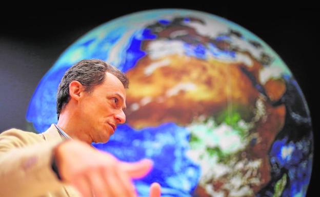 Pedro Duque conversa frente a una gran fotografía del planeta tal y como él lo vio a lo largo de sus viajes espaciales.