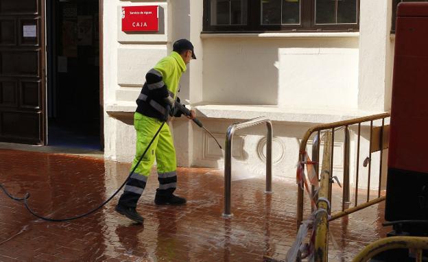 Un funcionario limpia una calle con agua a presión. 