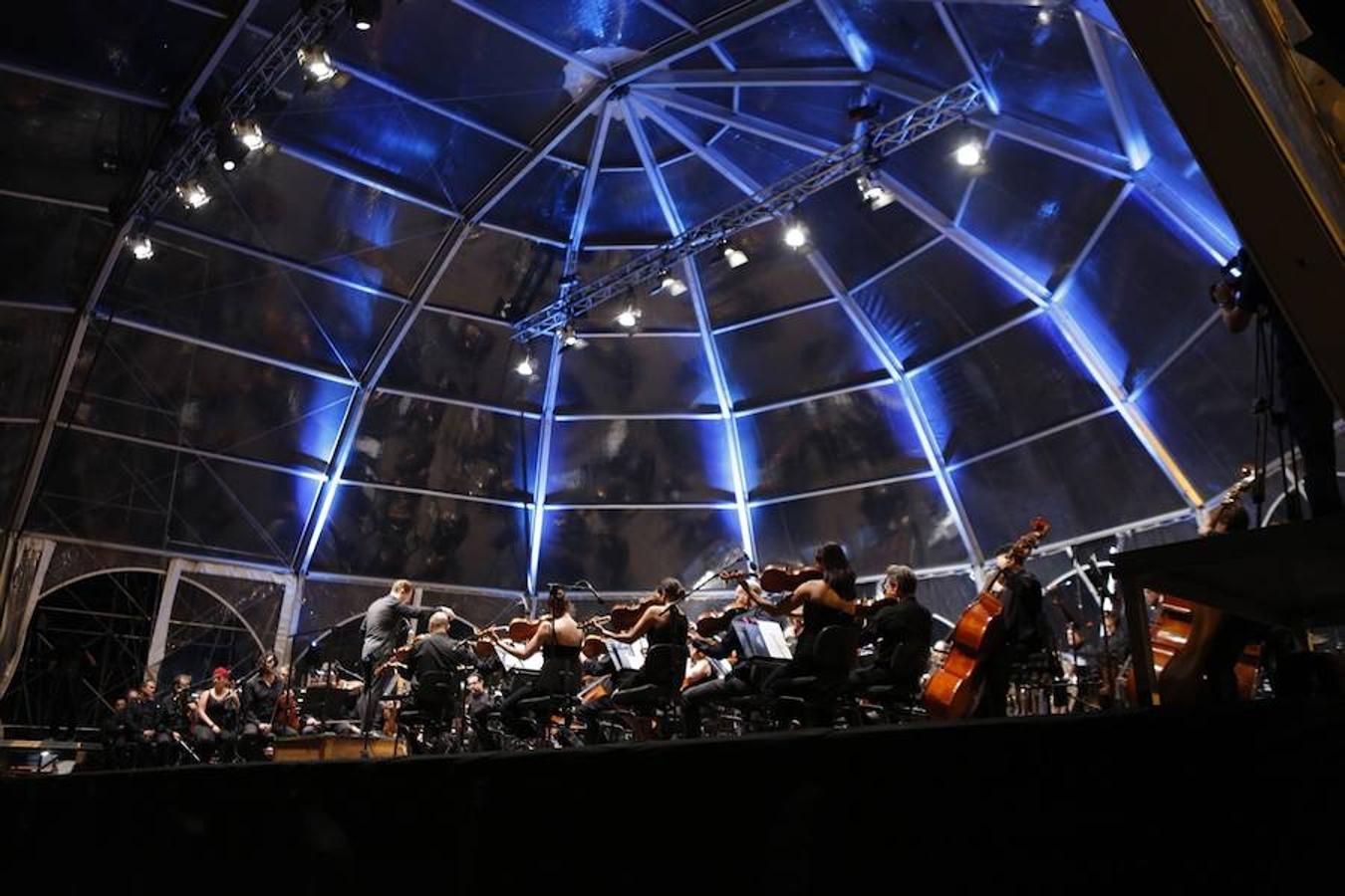 La Orquesta de Valencia hace historia junto al mar. Por primera vez, cierra la temporada en la playa de Las Arenas en un espectáculo para más de 1.000 personas. Un escenario de 300 metros y una cúpula transparente sirve de foco de atracción para el numeroso público congregado en la noche de este viernes en la playa. El concierto se ha bautizado con el nombre de 'Música i Aigua amb l'Orquesta de València'.