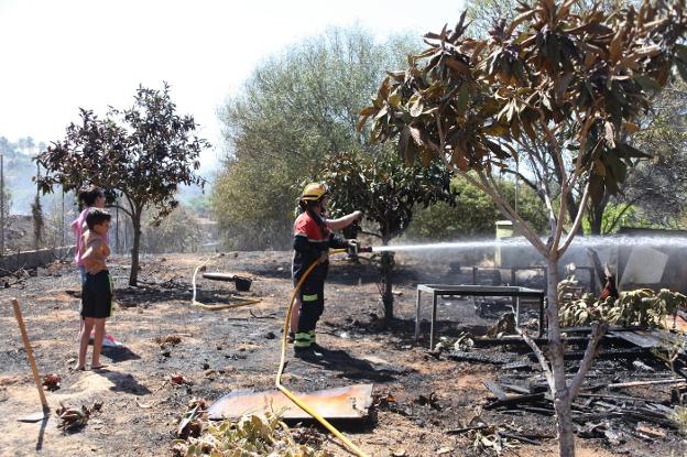 Un bombero sofoca el fuego en una propiedad ubicada en la entidad local menor de La Xara ante la atenta mirada de los vecinos. 