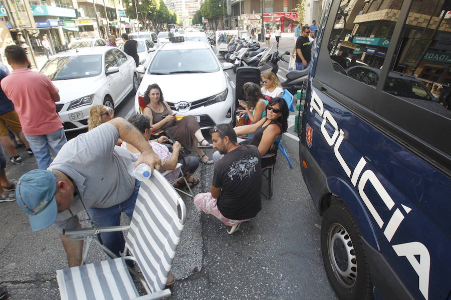 La huelga indefinida de taxistas en Valencia tiene como epicentro la calle Colón de Valencia. Allí, decenas de vehículo blancos están aparcados mientras los conductores tienen puesta toda la atención en la sede de Delegación del Gobierno. El único carril abierto es por el que circulan los autobuses de la EMT ante los taxistas que sentados en sillas plegables comentan, protestan y hace sonar el claxon. Unos conductores comparten café ante una mesa, mientras otros se muestran nerviosos con un cigarro en la mano. Ante la hora de comer, panes para los presenten y hasta se ha empezado un jamón entero. Las botellas de agua no han faltado ante las altas temperaturas que se registran en el centro de la ciudad.