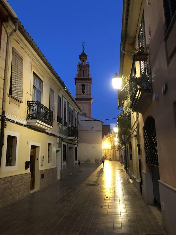 Es una de esas zonas poco conocidas de Valencia. El barrio de Campanar reúne todas esas características que se espera encontrar en un remoto y solitario pueblo, y no en plena urbe. Calles tranquilas, casas antiguas, fachadas con un encanto diseñado por el paso del tiempo. Recorrer sus aceras es pasear por un rincón de paz, ajeno al constante ajetreo de la ciudad. Una especie de paréntesis entre el tráfico, ruido y bullicio, en un lugar donde el reloj parece detenerse, mientras las sombras del atardecer se van colando por cada resquicio. Entre paredes blancas, tonalidades ocre, fuentes y ventanas que se asoman a décadas de historia, permanecen mosaicos en honor a lo que el pueblo fue. Azulejos que recuerdan al oficio hornero y la patrona, la Virgen de Campanar, cuelgan de paredes en las que los ladrillos soportan más años que peso. Casas, unas bajas y otras ilustres, que recuerdan un tiempo no tan lejano, muestras de la Valencia pasada rodeadas de la ciudad actual. 