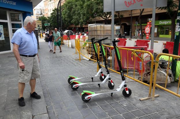 Un viandante observa tres unidades de los patinetes eléctricos repartidos por Valencia esta semana. 