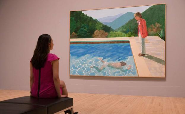 Una empleada posa con la obra del británico Hockney.