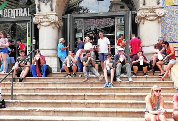 Turistas sentados en las escaleras del Mercado Central de Valencia. 