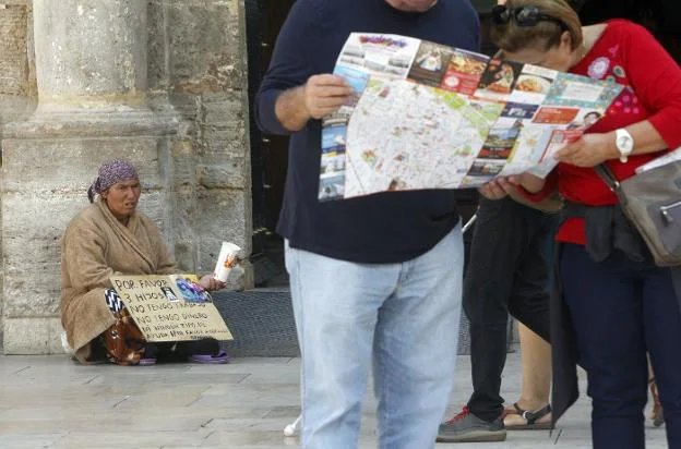  Contraste. Turistas observan un mapa mientras una mujer pide en centro de la ciudad. 