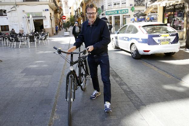 Grezzi camina por la calle Serranos con su bicicleta ante un coche de la Policía Local. 