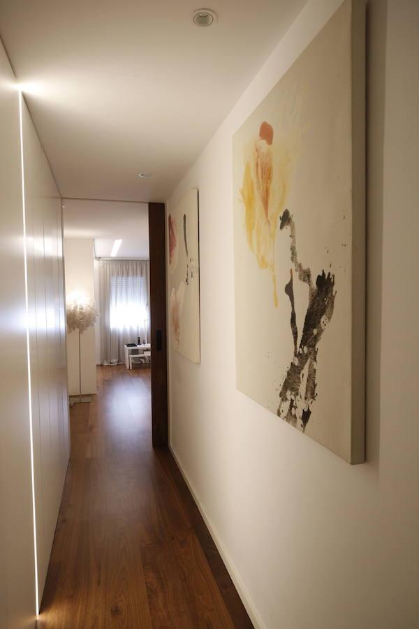 Las peticiones que Mariche Correcher planteó a la diseñadora creativa Carmen Bayarri estaban muy claras: que la casa tuviera muchos armarios, que la cocina y el salón estuviesen unidos pero a la vez se pudieran independizar y que la zona más tranquila de la casa albergara una suerte de suite en la que poder refugiarse después de la jornada de trabajo. Además le pidió que al entrar a la vivienda pudiera ver un ramo de flores. Con estas premisas, hace cuatro años se esbozó el proyecto en esta casa ubicada en una finca con carácter en pleno Ensanche valenciano. Para vestir el suelo escogieron madera de nogal, al igual que en las puertas que dividen las estancias. El resto de las puertas son blancas con las manivelas en negro y van de suelo a techo buscando potenciar la sensación de amplitud. En los baños instalaron porcelánico negro en el suelo que contrasta muy bien con el nogal. Carmen propuso ubicar junto a la entrada una escultura lacada flotante en rojo Ferrari que enmarca el espacio y permite ver el ramo de flores que reposa sobre la mesa del salón nada más entrar, que era uno de los deseos de la propietaria. La iluminación está integrada en la propia arquitectura. En lugar de obviar los pilares se decidió marcarlos de manera interna con filas de luz para ofrecer un ambiente casi escultórico. 