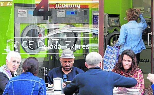 Un grupo de amigos toma café a las puertas de la lavandería, donde no para de entrar y salir gente durante todo el día.