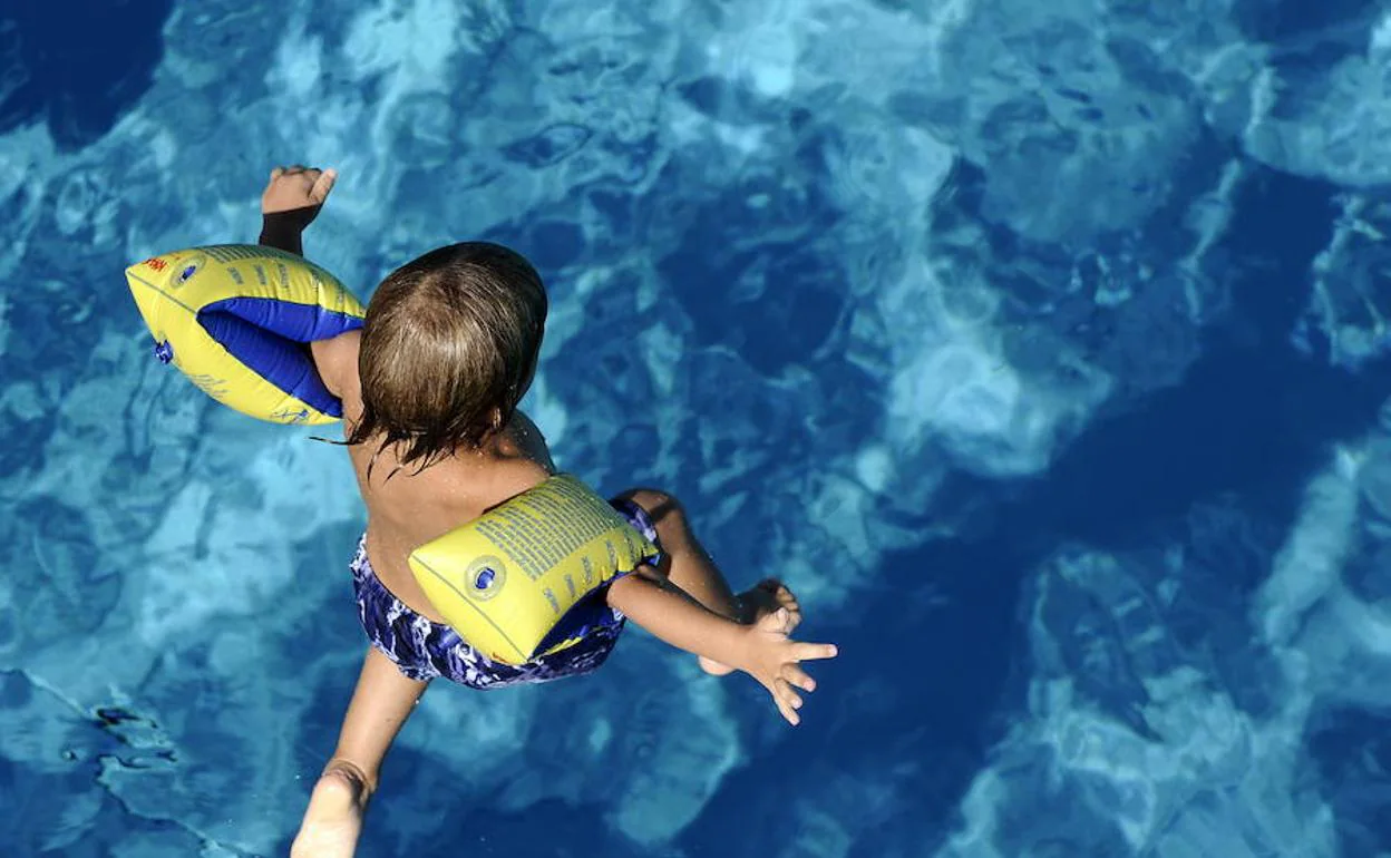 Un niño salta al agua en una piscina pública.