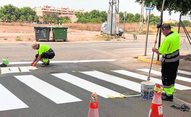 Dos operarios de la brigada municipal pintan un paso de peatones.