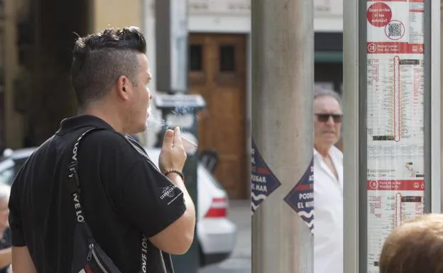 Un usuario fuma en una parada de la EMT. 