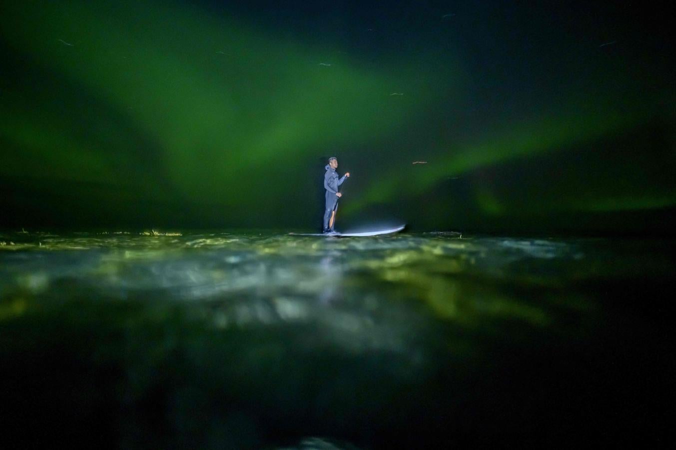 Edi Siswanto en su Paddle Board (SUP) bajo las luces del norte en Unstad, Islas Lofoten.