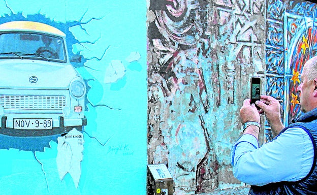 Imagen principal - Arriba, un turista fotografía el famoso mural de Birgit Kinder que representa a un 'trabi' atravesando el Muro, en la East Side Gallery. Abajo, a la izquierda, un grupo de jóvenes visita el Memorial del Muroun. A la derecha, el Memorial de Bernauerstrasse, que recuerda dónde estaba el Muro.