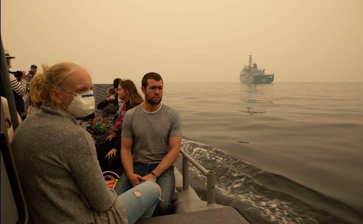 Un grupo de civiles navegan tras rescatados por la marina australiana tras quedar atrapados en una playa por los incendios forestales.