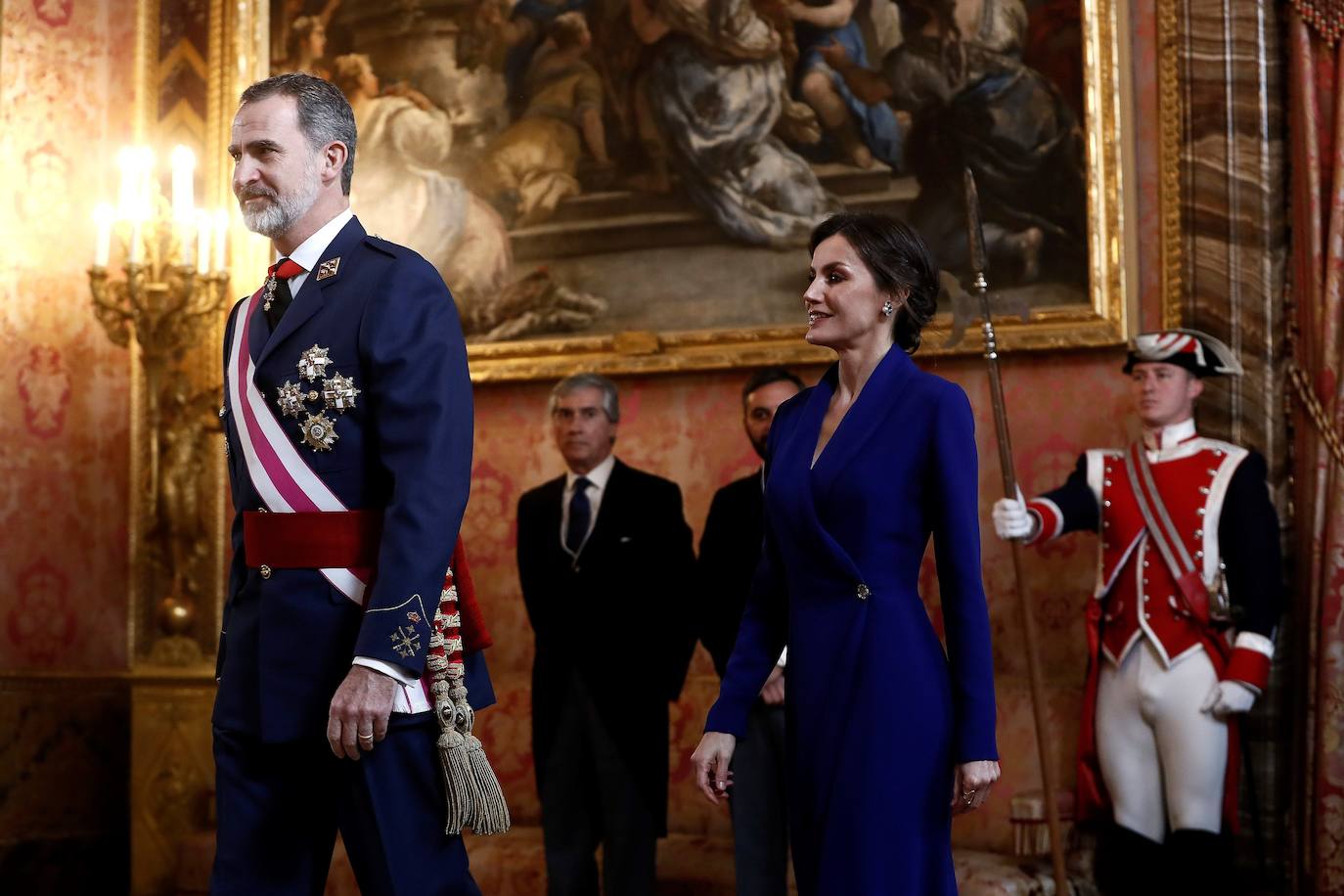 Felipe VI, acompañado por la Reina Letizia, ha presidido este lunes la ceremonia de la Pascua Militar en el Palacio Real. Para la ocasión, Doña Letizia ha elegido un elegante vestido de estilo esmoquin en azul intenso. La Reina ha combinado el diseño, largo hasta los pies, con unos zapatos stilettos en color negro y un peinado recogido acabado en un moño bajo.