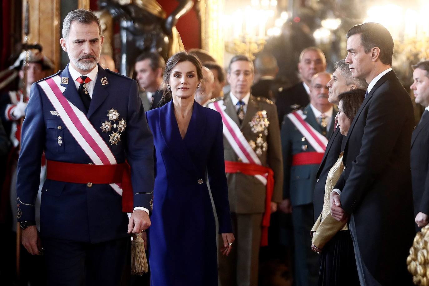 Felipe VI, acompañado por la Reina Letizia, ha presidido este lunes la ceremonia de la Pascua Militar en el Palacio Real. Para la ocasión, Doña Letizia ha elegido un elegante vestido de estilo esmoquin en azul intenso. La Reina ha combinado el diseño, largo hasta los pies, con unos zapatos stilettos en color negro y un peinado recogido acabado en un moño bajo.