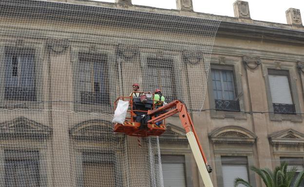 Dos obreros colocan la nueva red anticascotes desde la cesta de una grúa en la fachada de Zapadores.