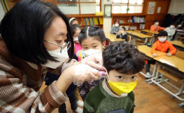 Un maestro mide las temperaturas de un alumno de primaria el primer día de clases después de las vacaciones de invierno.