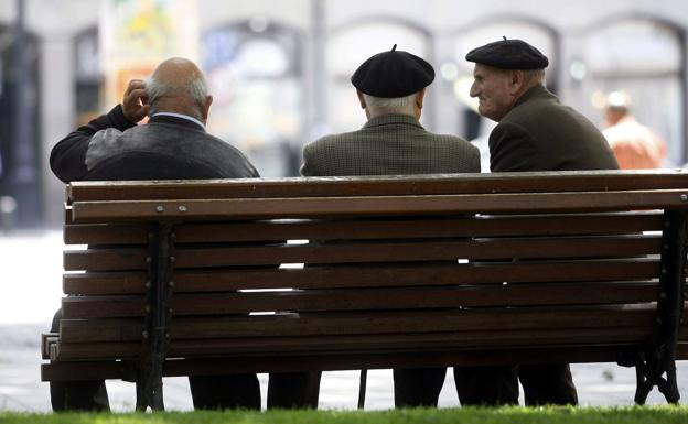 Tres jubilados charlan sentados en un banco. 