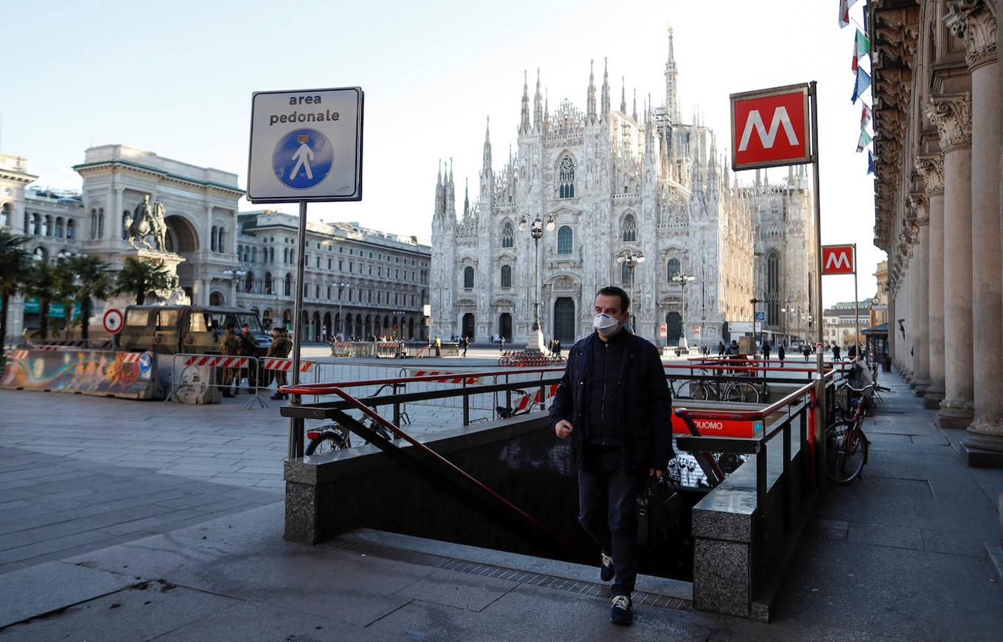 Un hombre con una máscara protectora camina junto a una plaza del Duomo casi desierta.