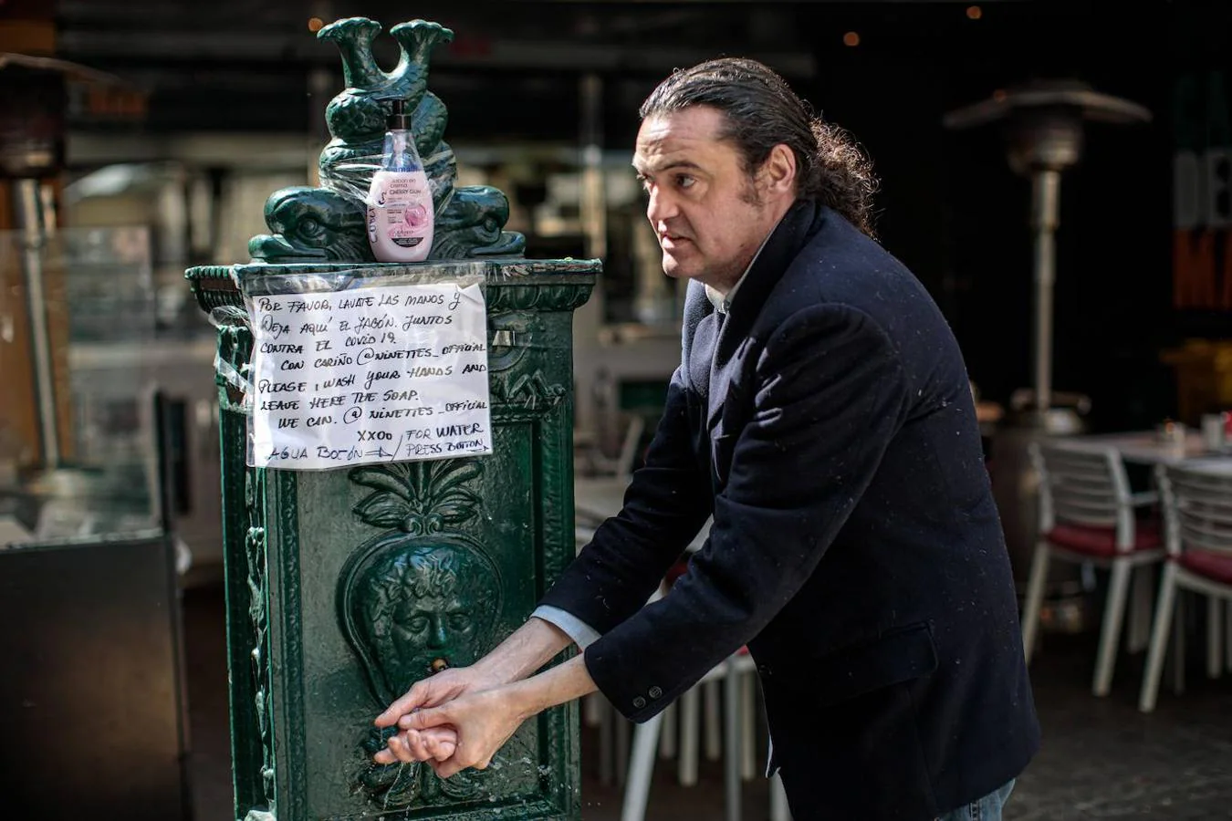 Un hombre se lava las manos en una fuente de Valencia donde han dejado un dispensador de jabón y un cartel donde puede leerse 'Por favor, lávate las manos y deja aquí el jabón. Juntos contra el COVID-19'. 