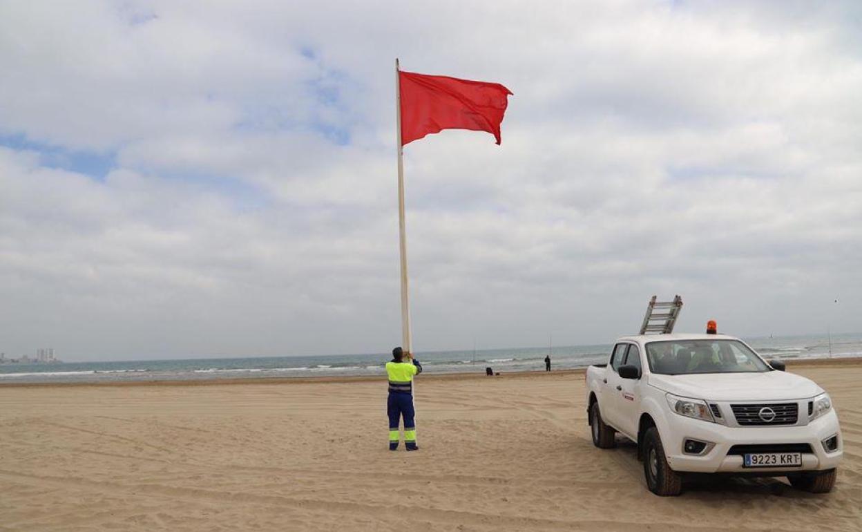 Un operario coloca una bandera roja en una playa de Cullera.