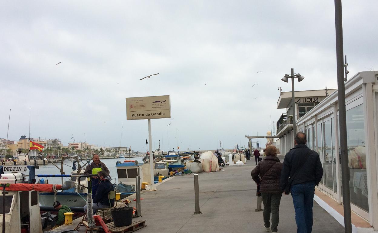 Unos pescadores realizan tareas en sus barcas en el puerto y unos turistas pasean, antes del estado de alarma.