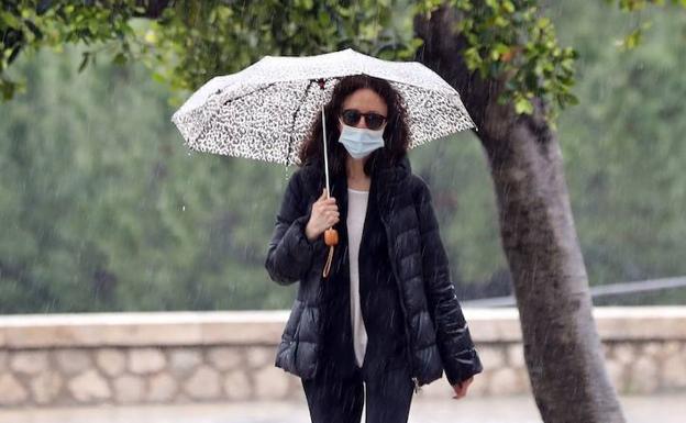 Una persona pasea con mascarilla y paraguas en Valencia. 