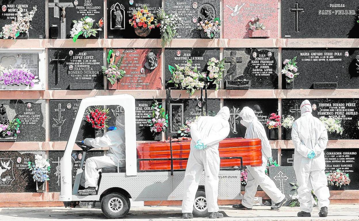 Personal del cementerio del Cabanyal transporta un féretro durante un entierro al que han podido asistir tres familiares, el máximo autorizado.