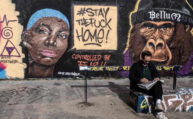 Un hombre descansa junto a un grafiti que indica la necesidad de quedarse en casa