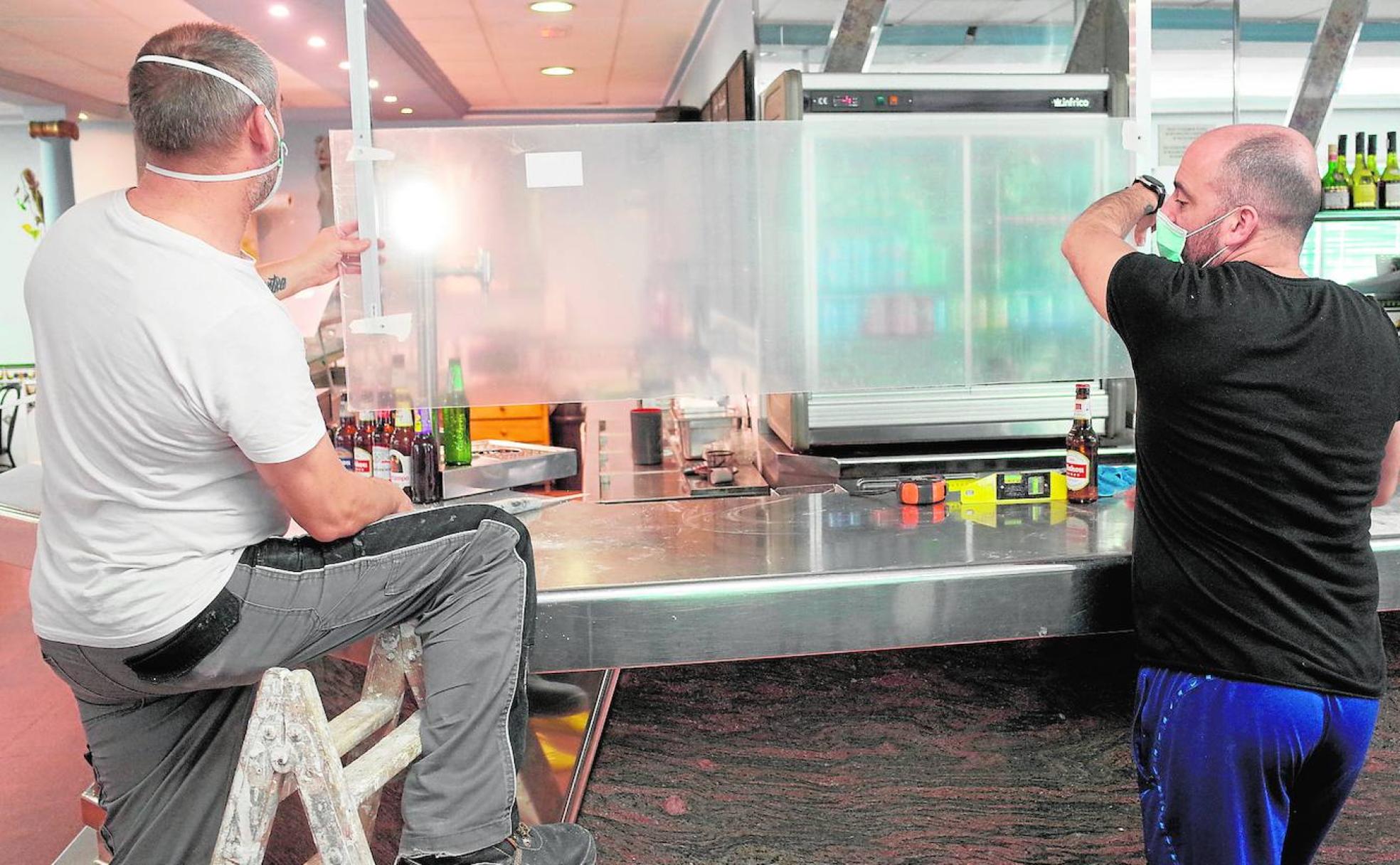 José Coné y un trabajador colocan un panel de policarbonato en la barra del restaurante Nueva Mutua en el polígono industrial Vara de Quart.