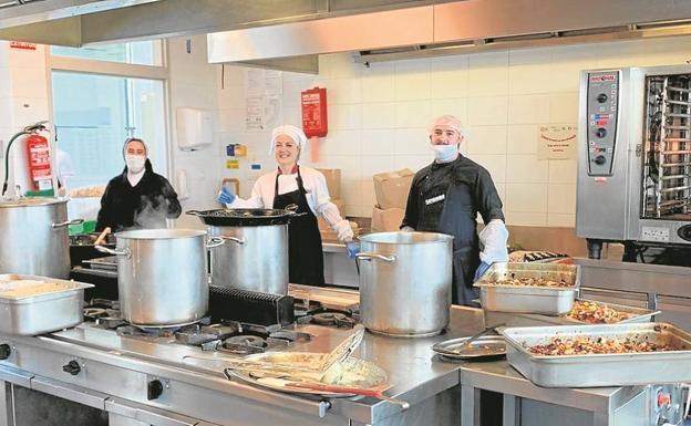 Dos cocineras y un cocinero posan un momento durante la preparación de la comida antes de empezar a repartirla. 