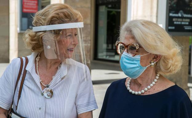 Dos mujeres conversan protegidas por mascarilla y pantalla en una avenida de Zaragoza. 