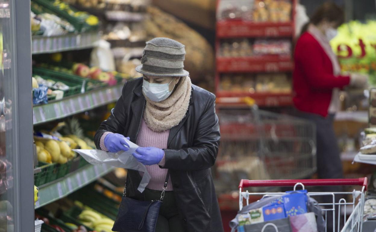 Una mujer, con mascarilla, en la sección de frutas y verduras de un supermercado. 